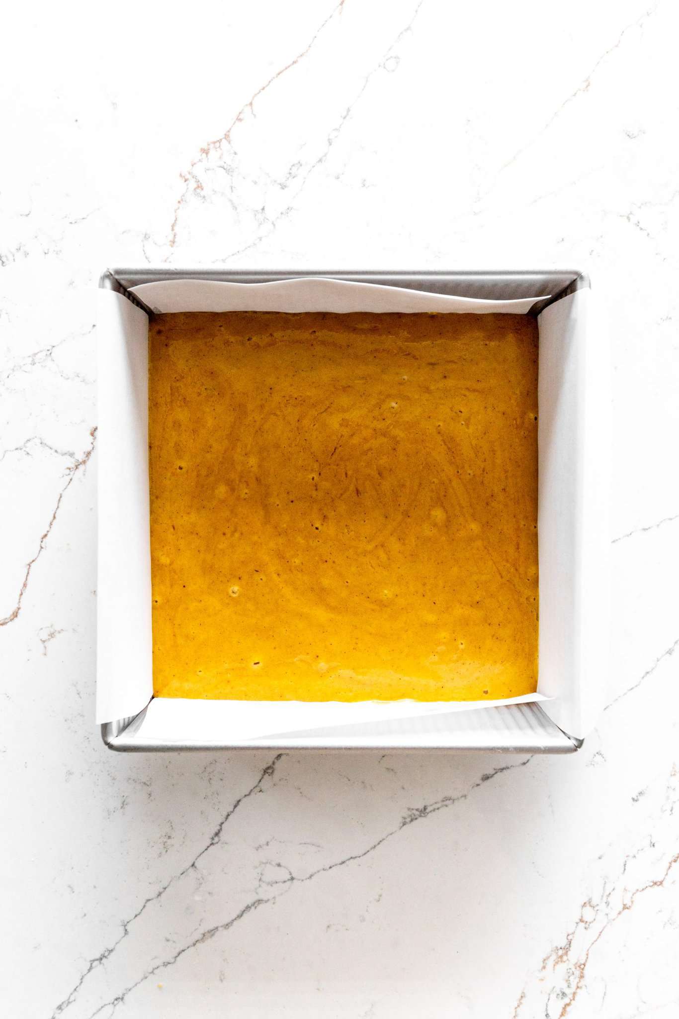 Square, parchment-lined pan filled with pumpkin cake batter.