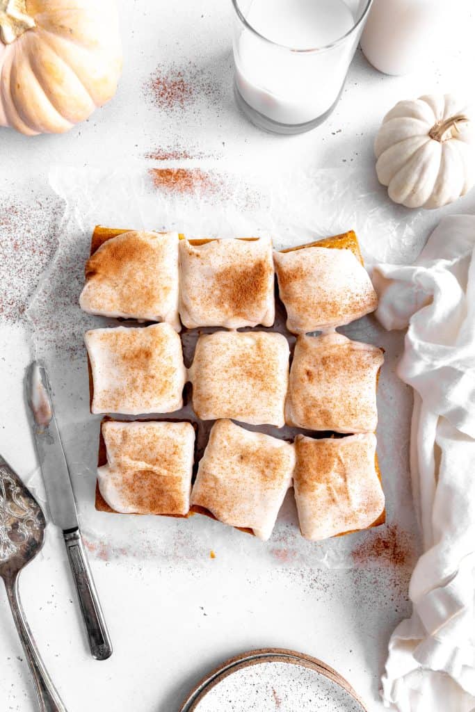 Frosted pumpkin bars, a glass of milk, a stack of plates and a knife.