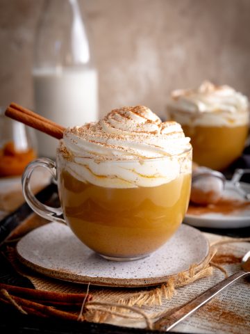 Pumpkin spice latte in a glass mug topped with whipped cream and cinnamon.