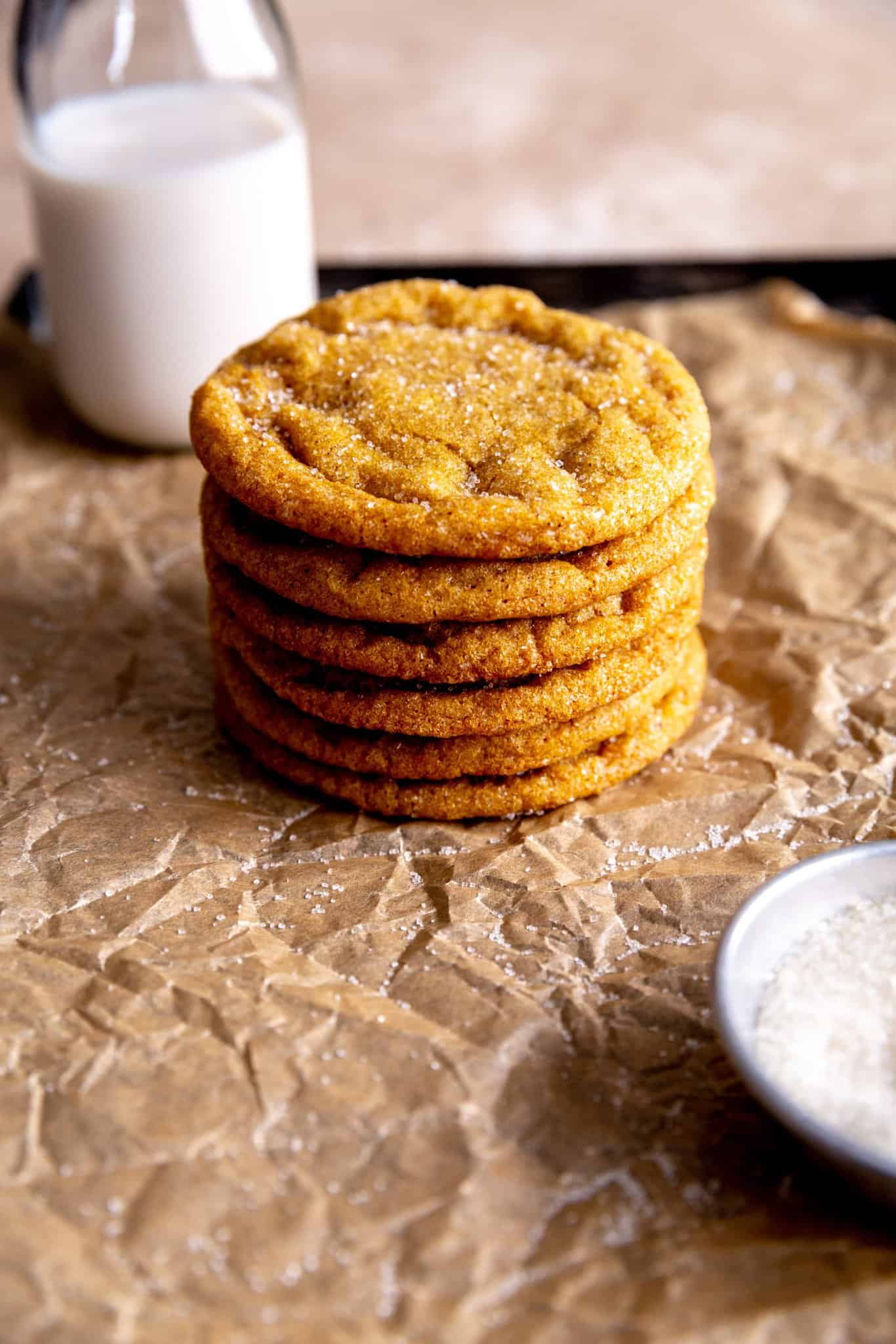 Stack of pumpkin sugar cookies in front of a jug of milk.