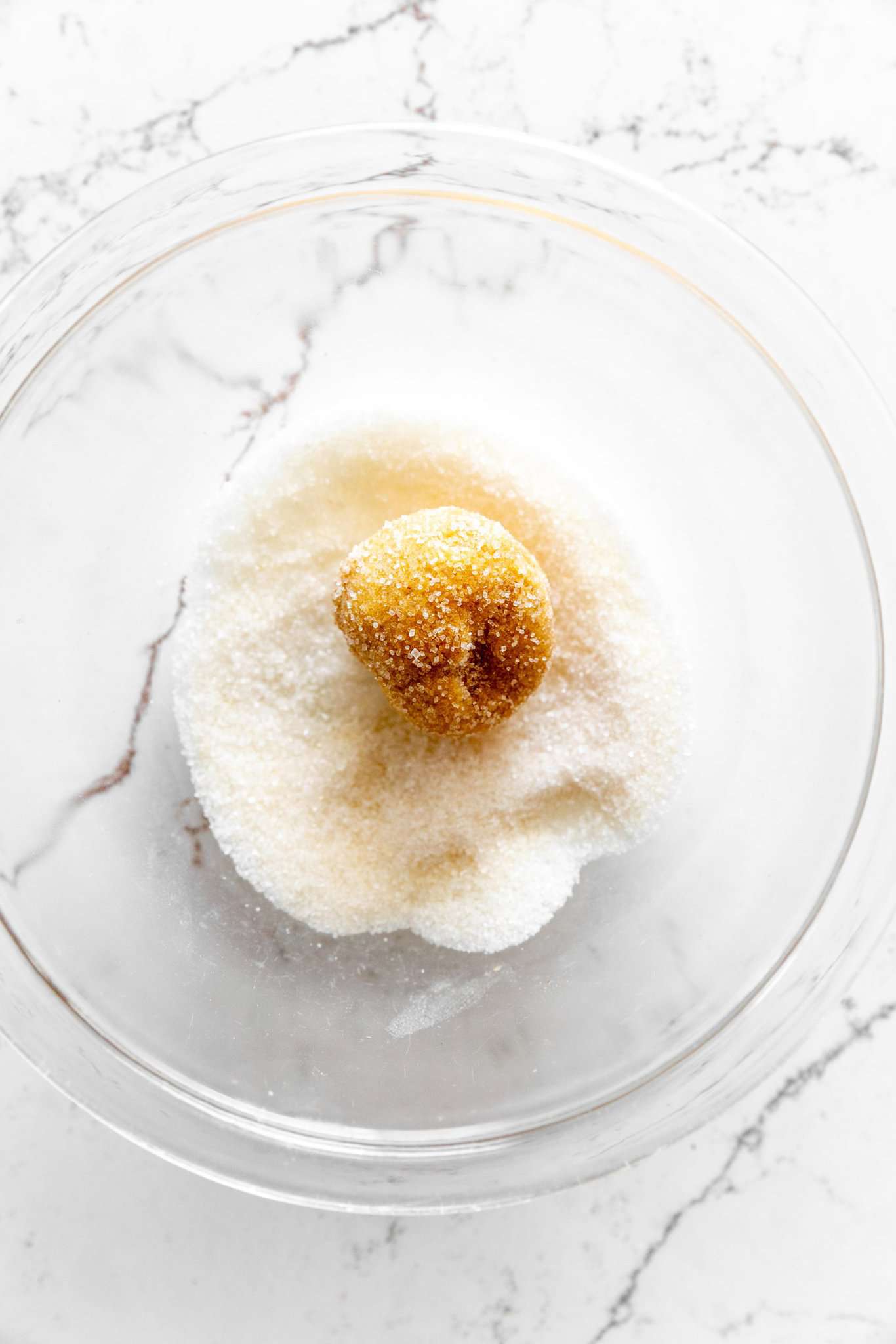 Ball of pumpkin sugar cookie dough in a ball of granulated sugar.