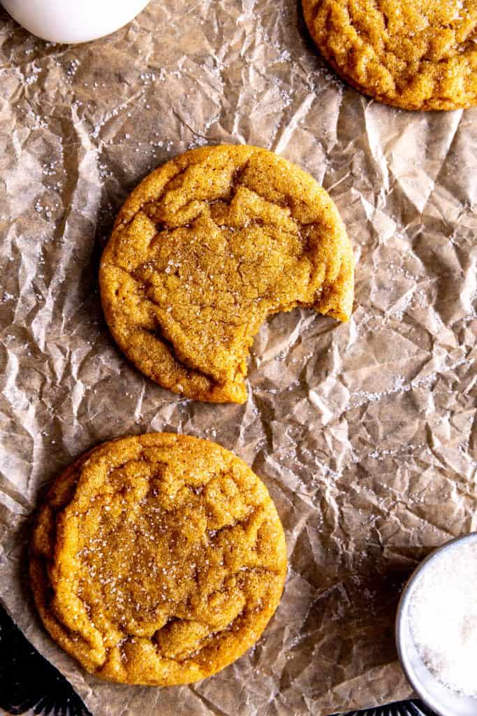 Pumpkin sugar cookie with a bite taken out of it with more cookies and a jug of milk.