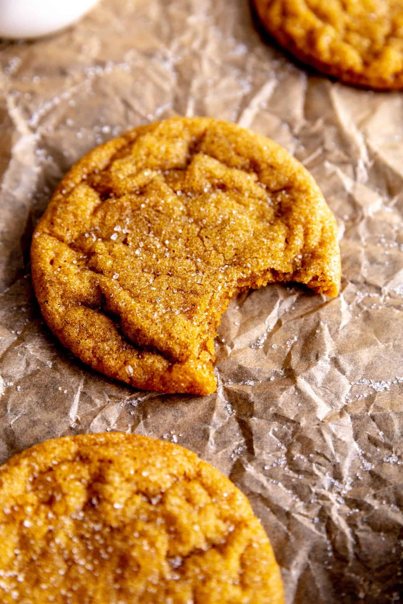 Pumpkin sugar cookie with a bite taken out of it and a jug of milk.