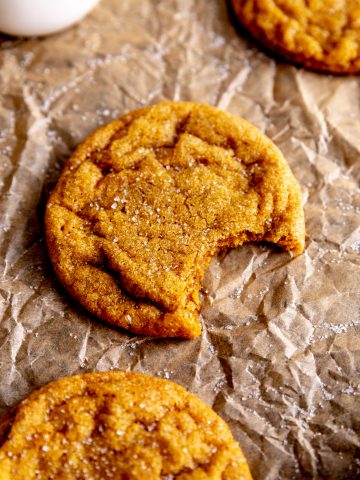 Pumpkin sugar cookie with a bite taken out of it and a jug of milk.