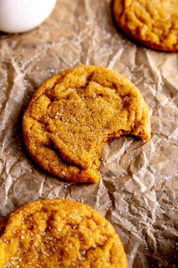 Pumpkin sugar cookie with a bite taken out of it and a jug of milk.