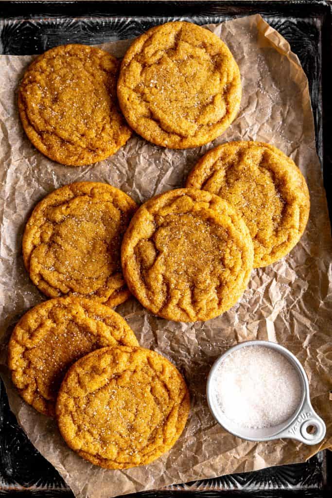 Vegan sugar cookies on a baking sheet with a cup of granulated sugar.