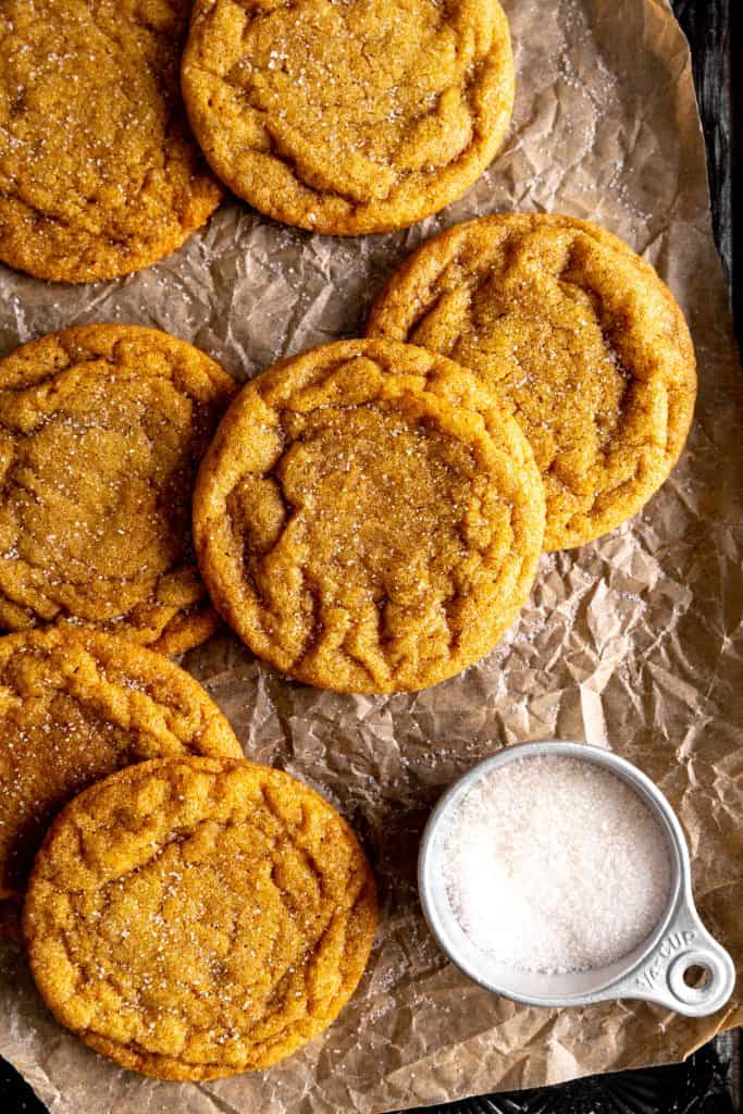 Pumpkin sugar cookies on a baking sheet with a cup of sugar.