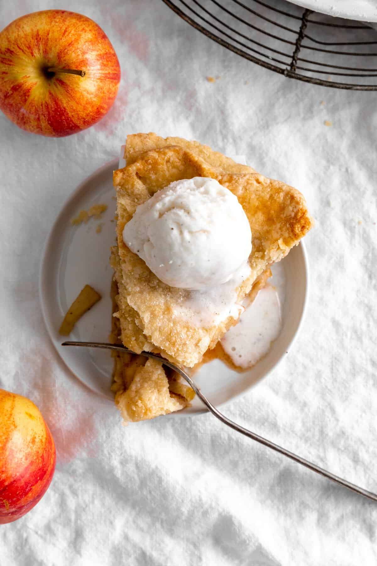 Fork cutting into a slice of apple pie topped with vanilla ice cream.