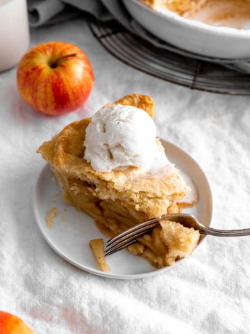 Fork cutting into slice of apple pie topped with vanilla ice cream.