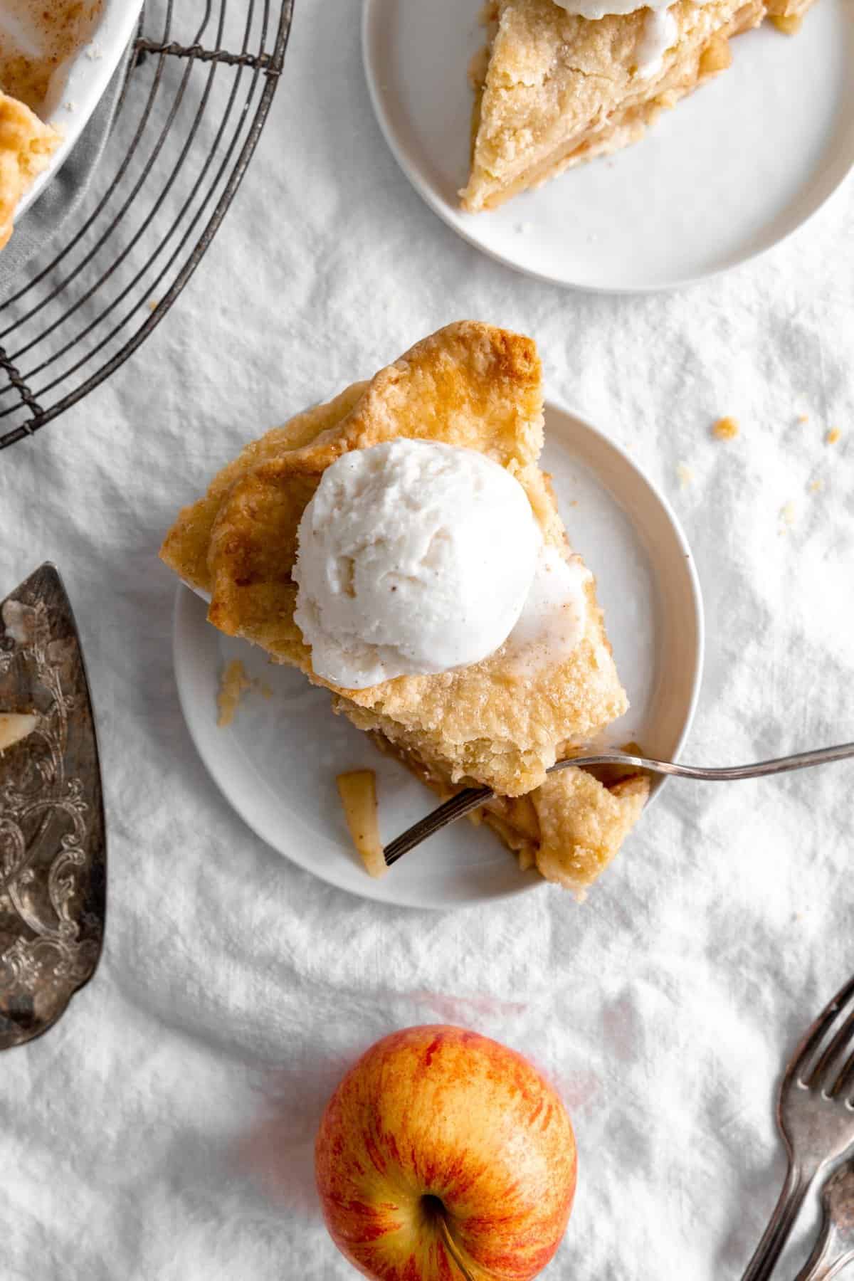 Fork cutting into slice of apple pie topped with a scoop of vanilla ice cream.