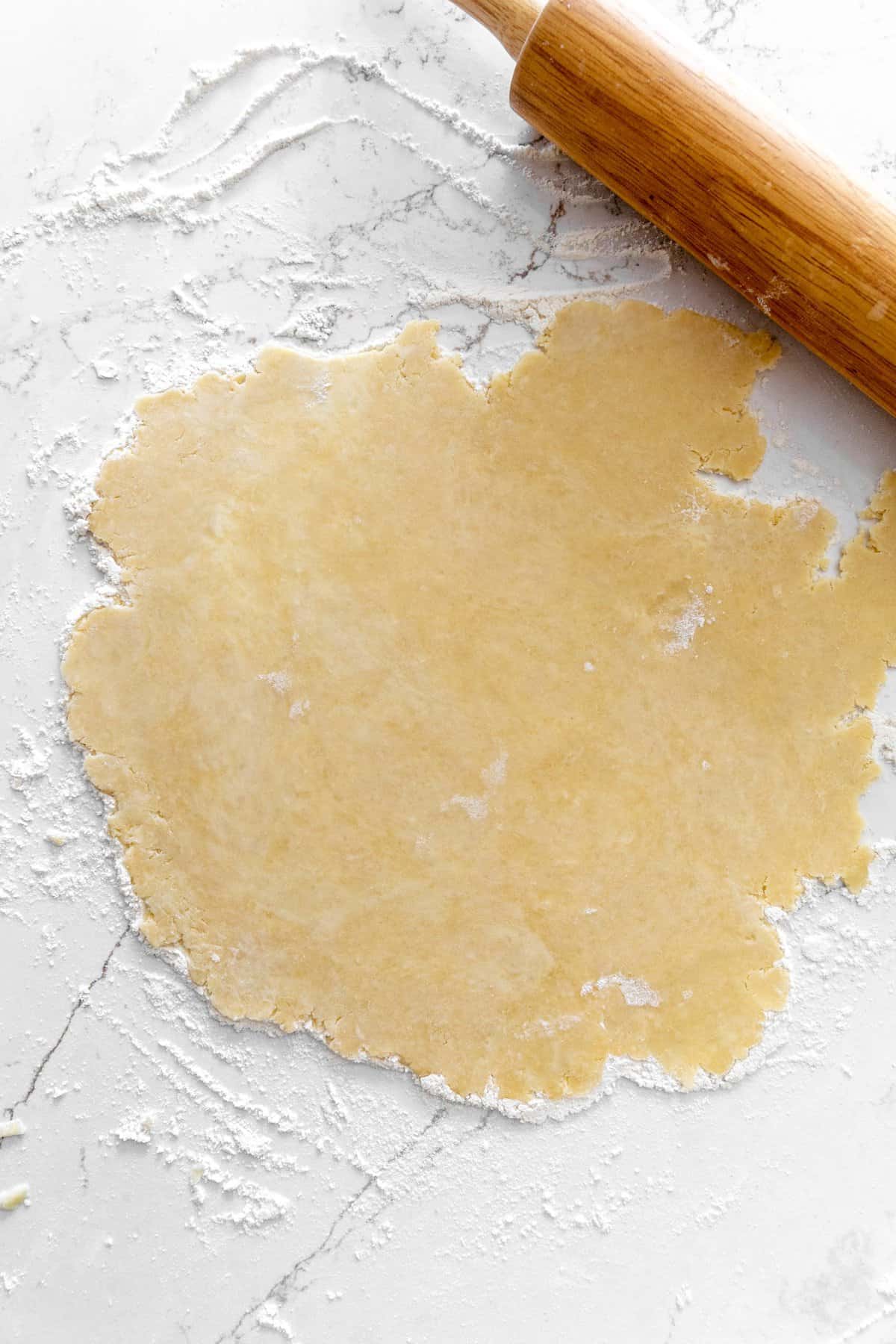 Pie crust dough rolled out on a marble surface and a rolling pin.