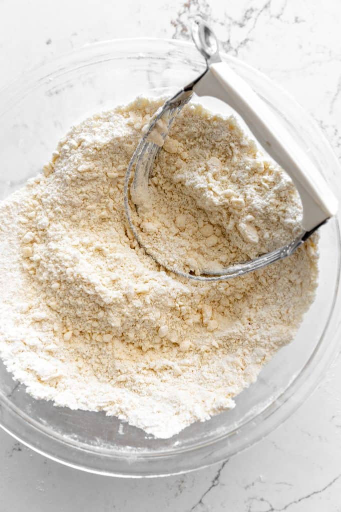 Flour and butter in a glass bowl with a pastry cutter.