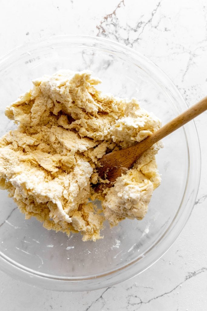 Pie crust dough in a glass bowl with a wooden spoon.