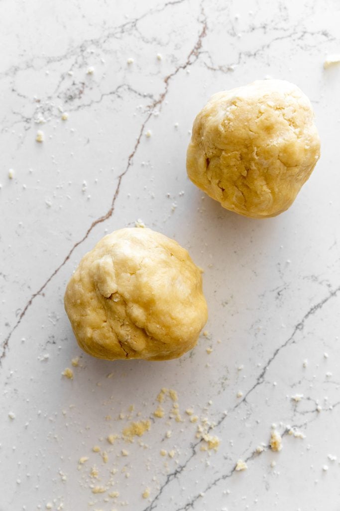 Two balls of pie crust dough on a marble surface.