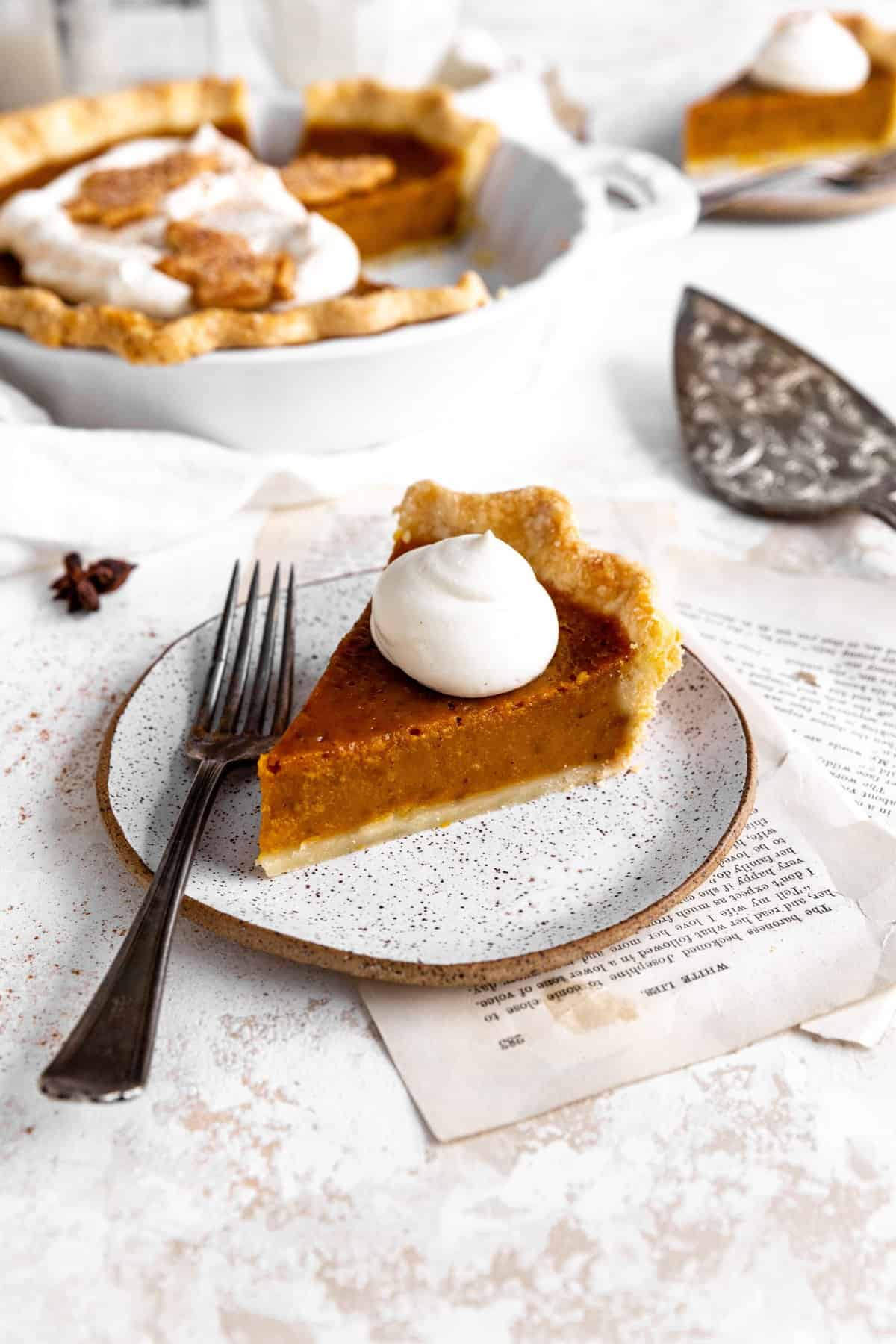 Slice of pumpkin pie topped with whipped cream on a plate with a fork.