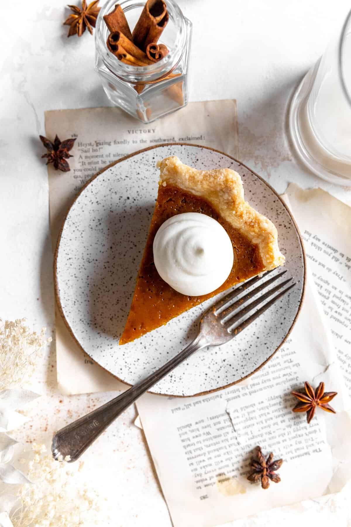 Slice of pumpkin pie topped with whipped cream on a plate with a fork.