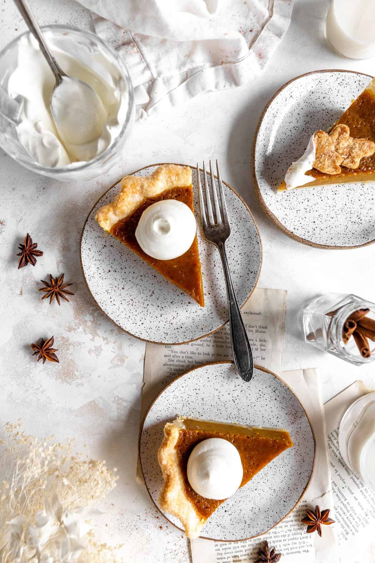 Three slices of pumpkin pie topped with whipped cream on plates.