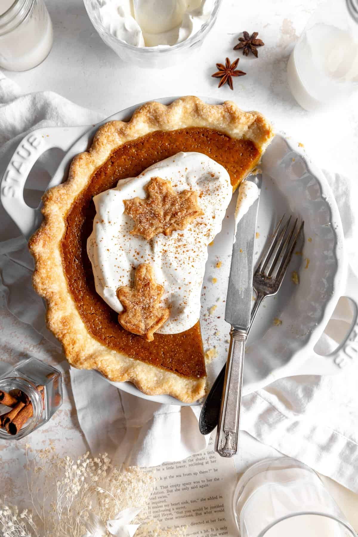 Pumpkin pie with pieces missing and cutlery in the pie plate.