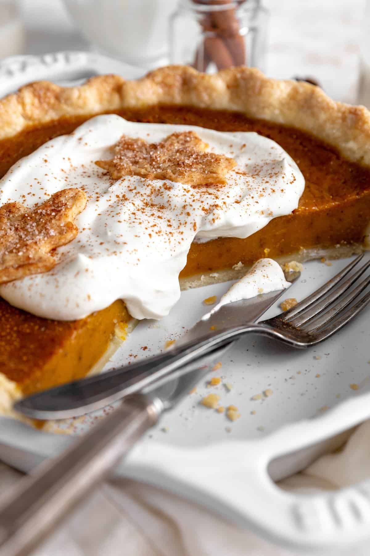 Pumpkin pie with pieces missing and cutlery in the pie plate.