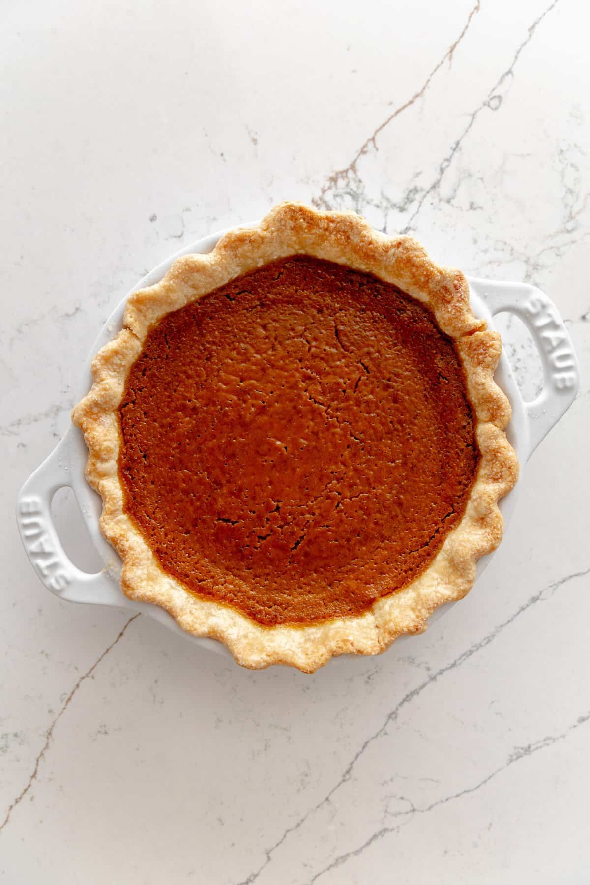 Baked pumpkin pie on a white marble surface.