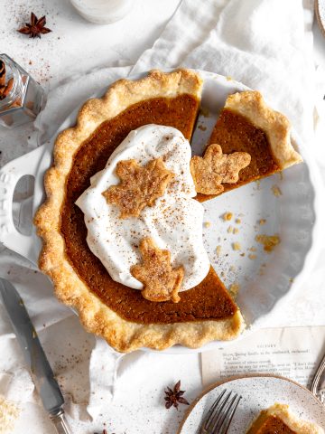 Pumpkin pie topped with whipped cream, a cup of milk and cinnamon sticks.