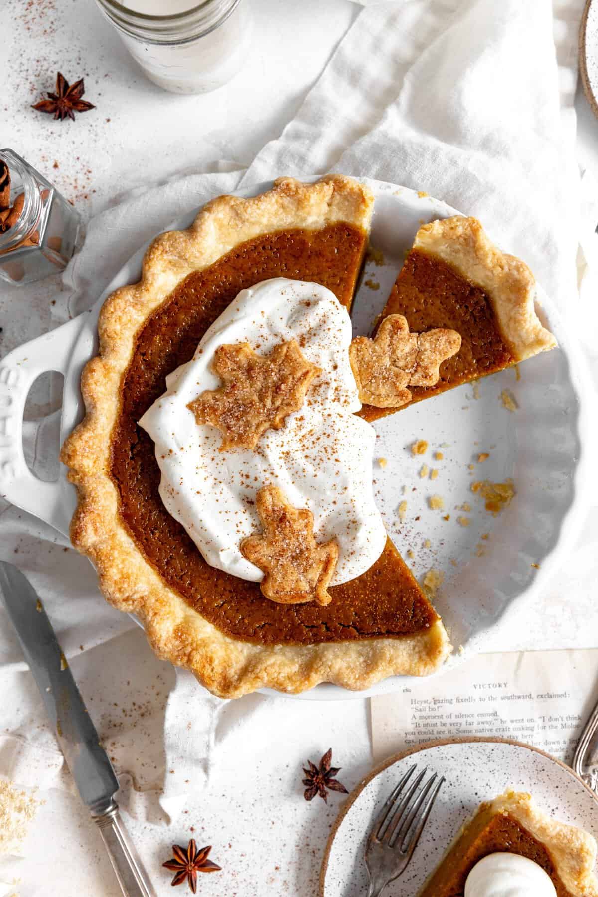 Pumpkin pie topped with whipped cream, a cup of milk and cinnamon sticks.