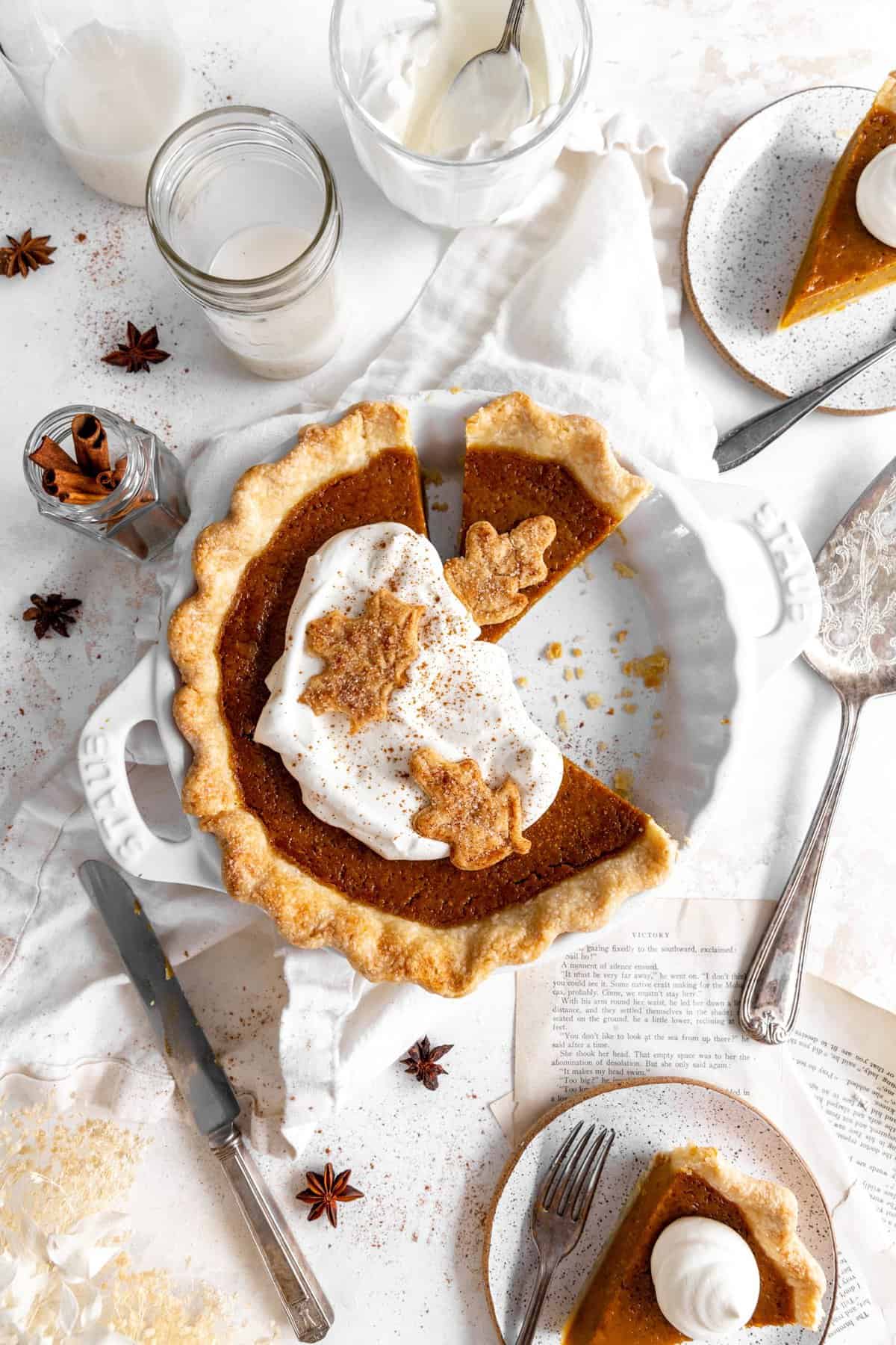 Pumpkin pie topped with whipped cream and two slices on plates.