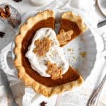 Pumpkin pie topped with whipped cream, a glass of milk and cutlery.