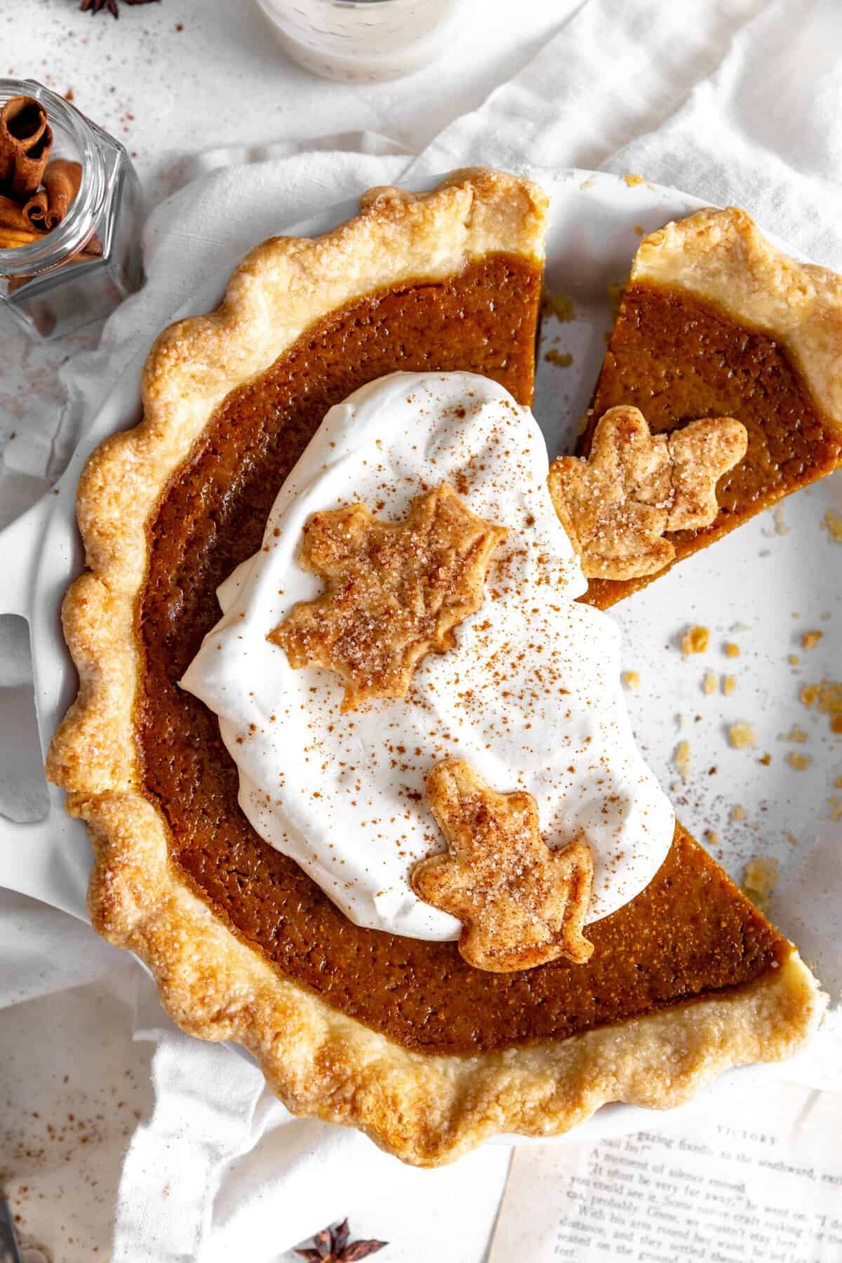 Pumpkin pie topped with whipped cream and a jar of cinnamon sticks.