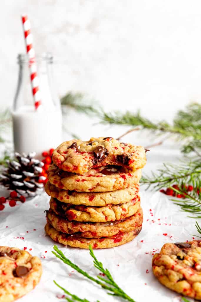 Stack of candy cane chocolate chip cookies and a jug of milk with a straw.