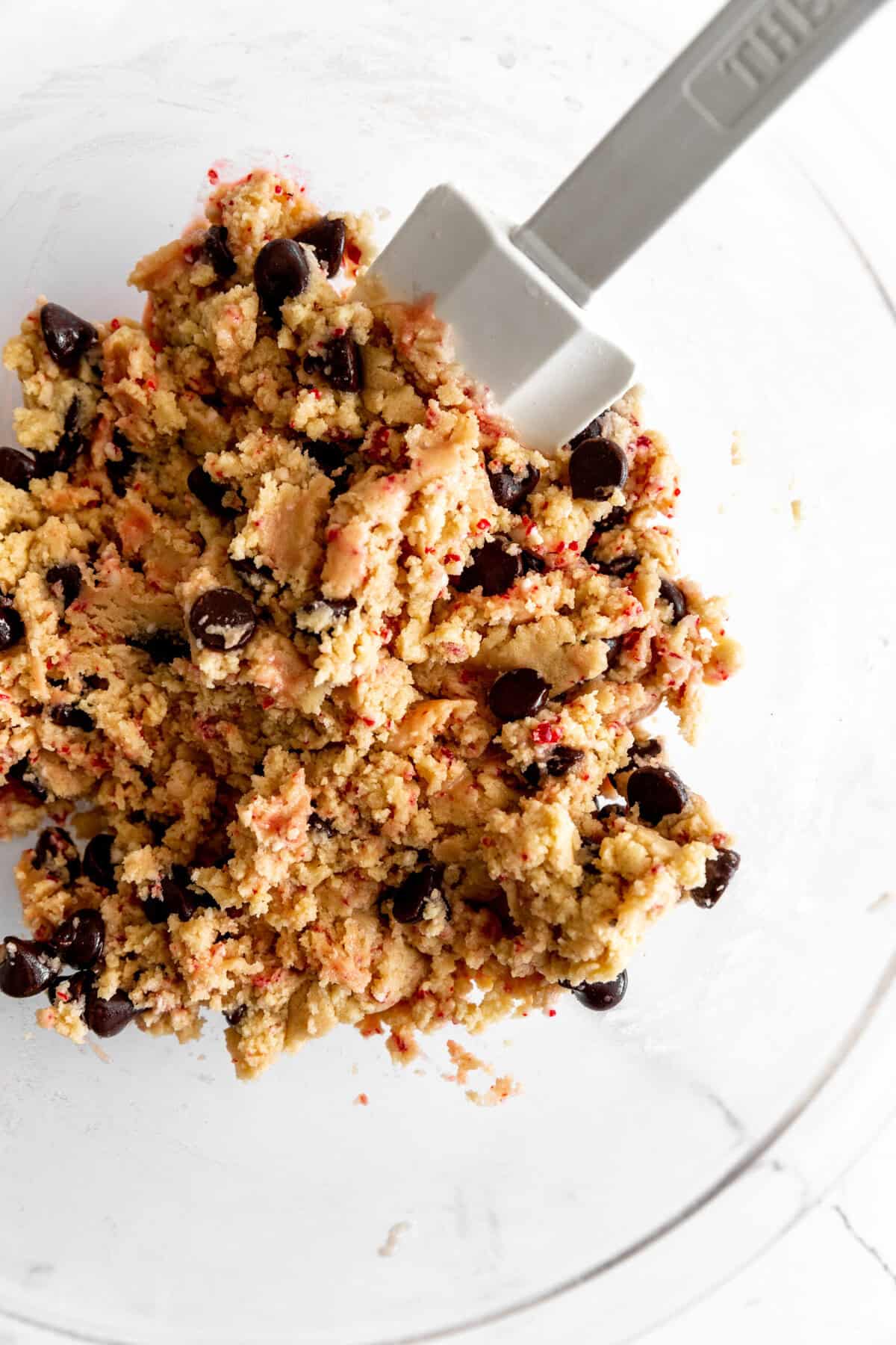 Vegan candy cane chocolate chip cookie dough in a glass bowl with a rubber spatula.