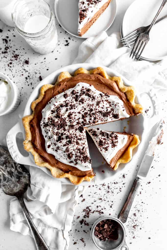 Chocolate fudge pie with a slice missing, a glass of milk and a knife.