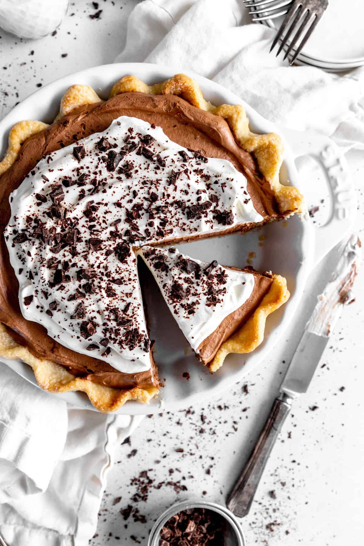 Chocolate fudge pie with a slice missing, a cup of chopped chocolate and a knife.