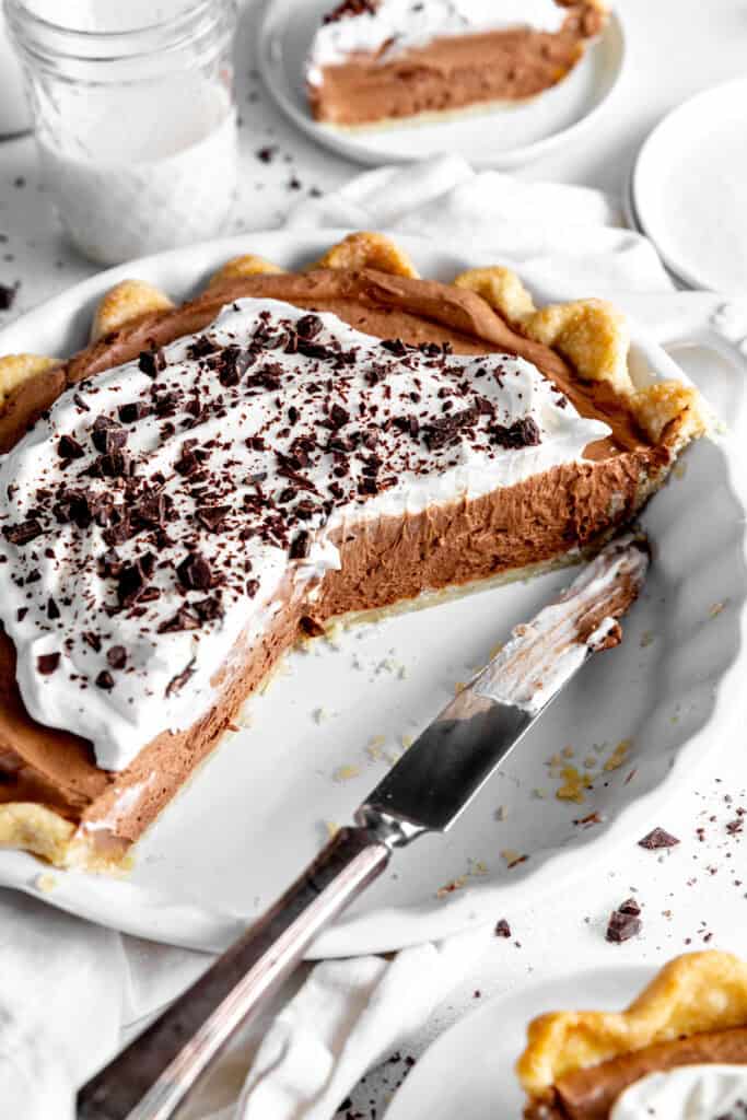 Half of a chocolate fudge pie in a white dish with a knife in front of a glass of milk.