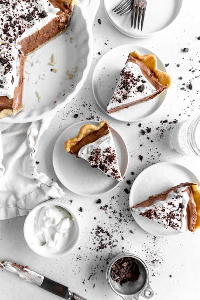 Slices of chocolate fudge pie on white plates, a cup of cream and a glass of milk.