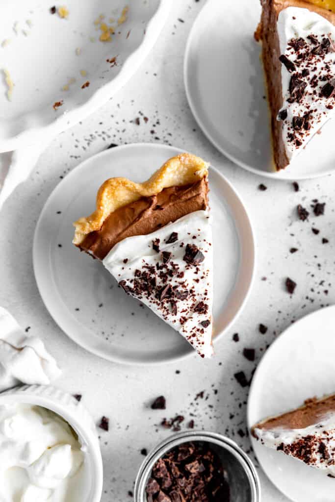 Slice of chocolate fudge pie on a white plate and a cup of chopped chocolate.