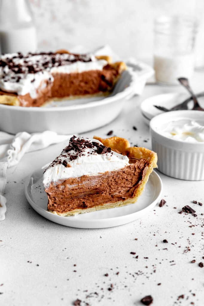 Slice of chocolate fudge pie in front of a chocolate pie and a jug of milk.