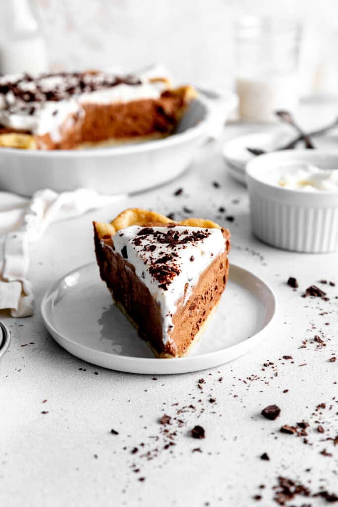 Slice of chocolate fudge pie in front of a chocolate pie and a jug of milk.