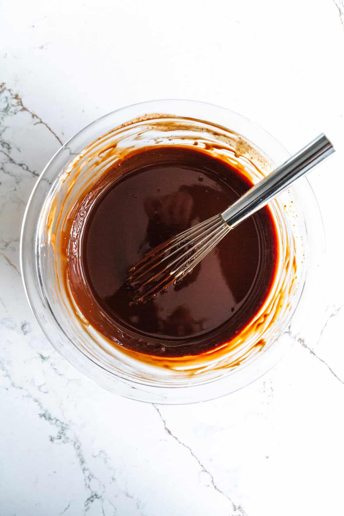 Glass bowl filled with melted chocolate and a wire whisk.