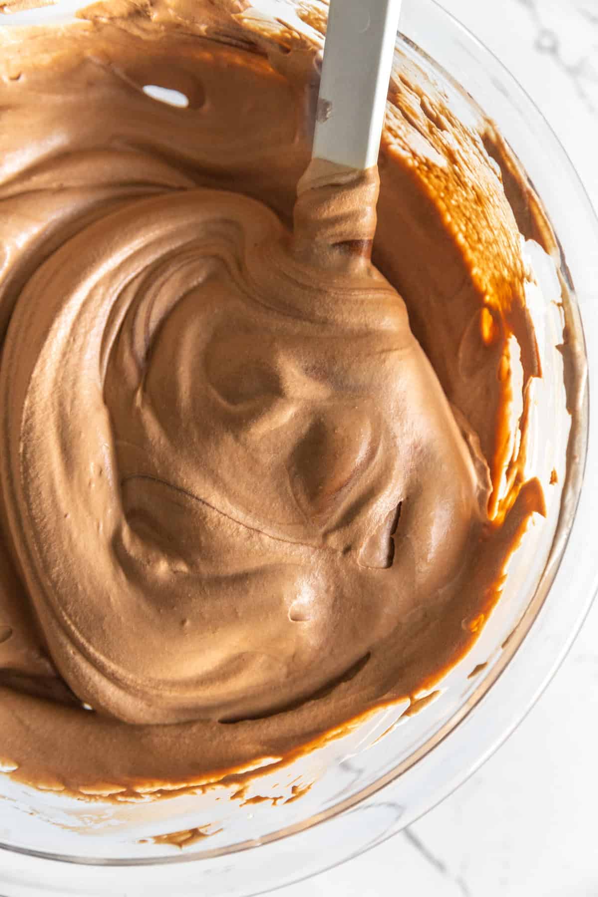 Chocolate-cream pie filling in a glass bowl with a rubber spatula.