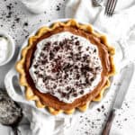 Chocolate fudge pie, a glass of milk, a stack of plates and a knife.