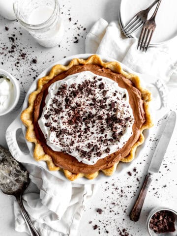 Chocolate fudge pie, a glass of milk, a stack of plates and a knife.