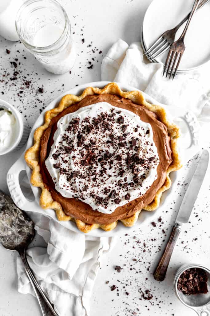 Chocolate fudge pie, a glass of milk, a stack of plates and a knife.