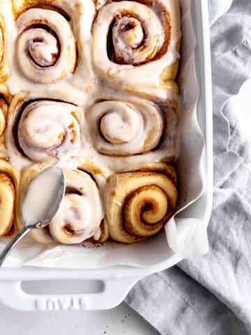 Spoon spreading icing on a pan of cinnamon rolls.