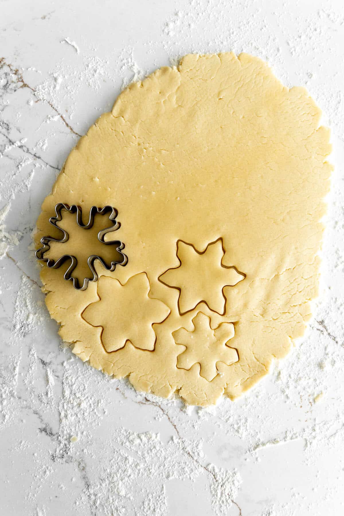 Snow flake cookie cutter cutting into rolled out sugar cookie dough.