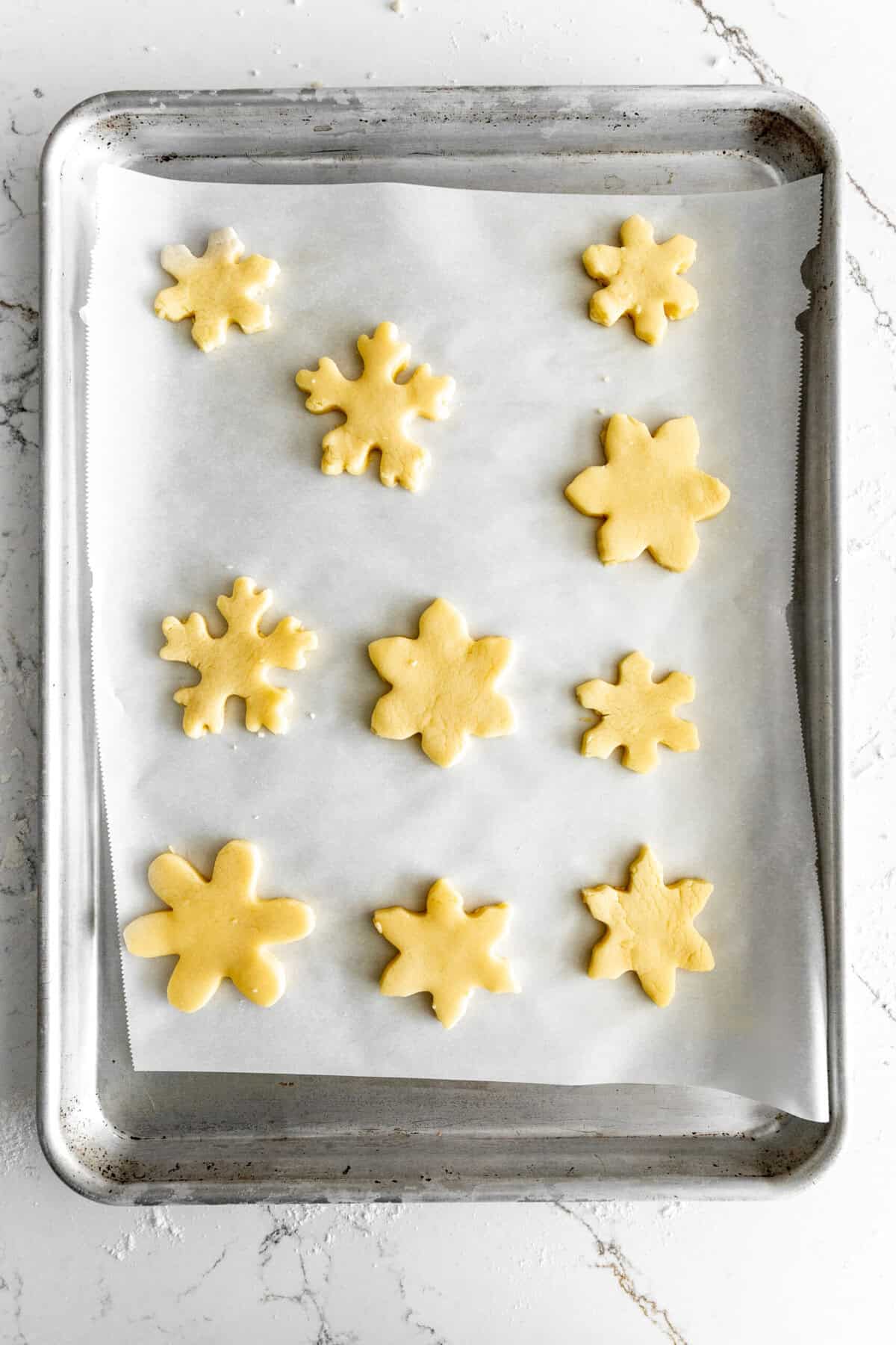 Unbaked snowflake sugar cookies on a baking sheet.