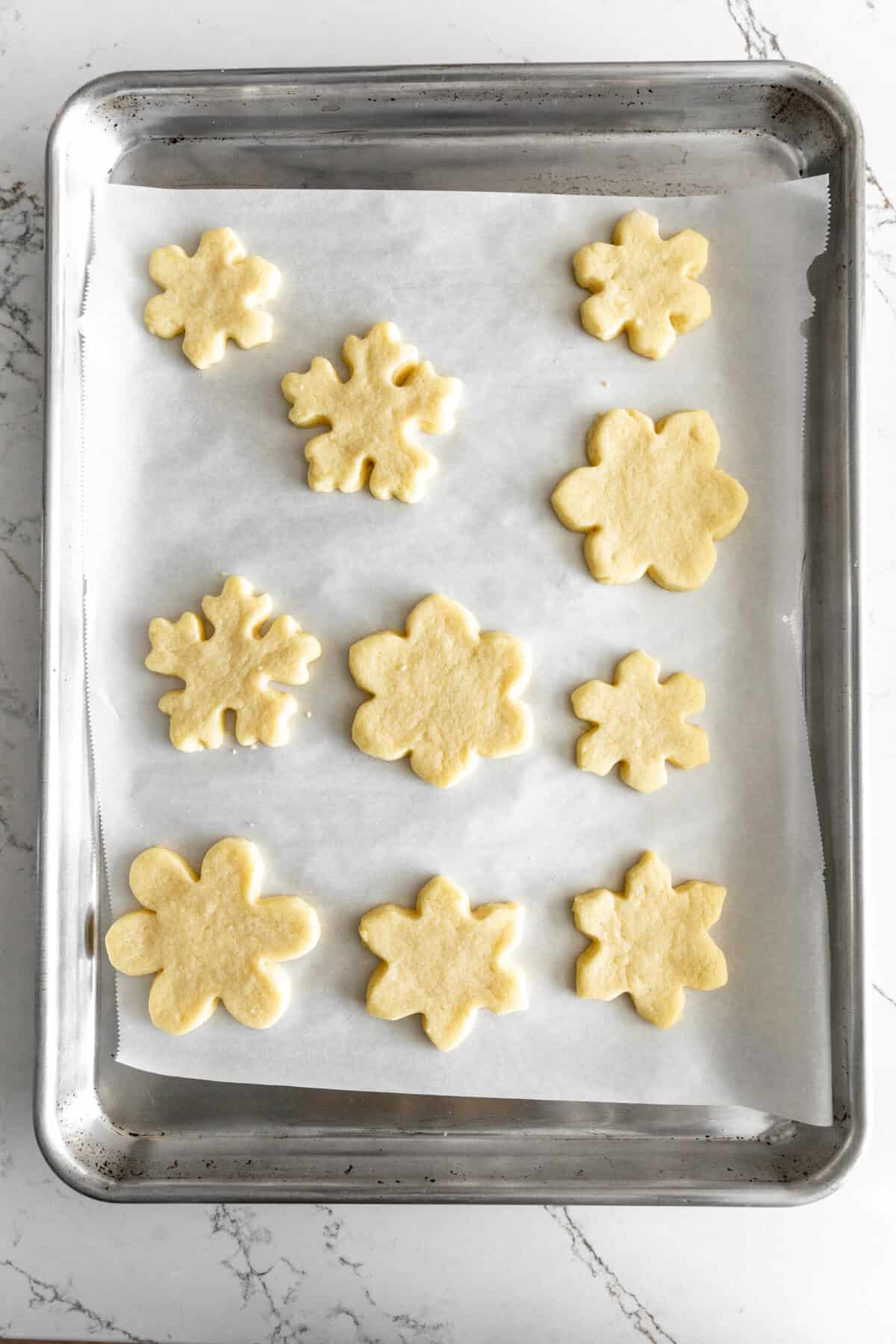 Baked snowflake sugar cookies on a baking sheet.