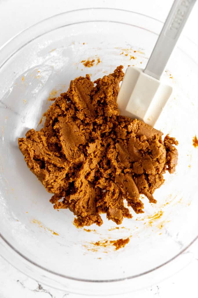 Gingerbread cookie dough in a glass bowl with a rubber spatula.