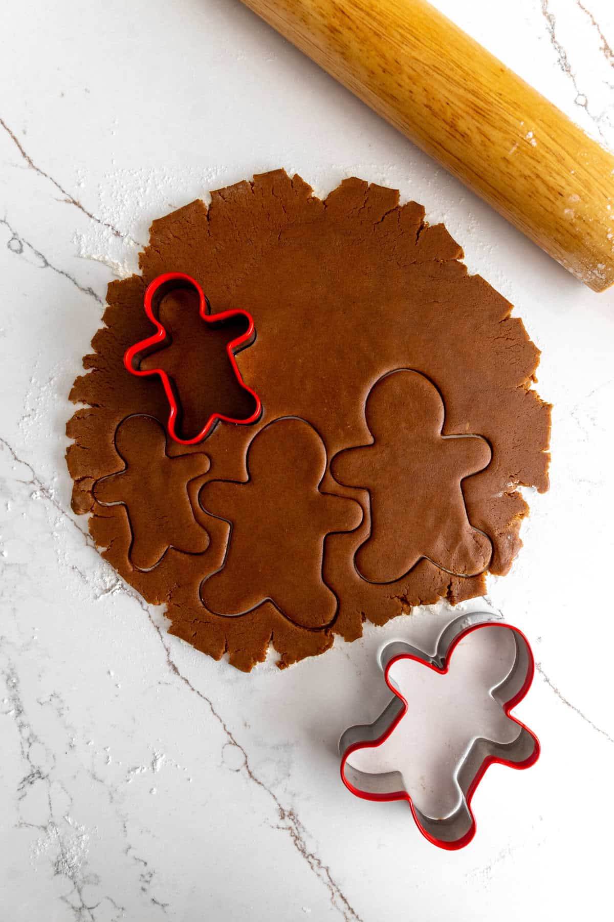 Cookie cutters cutting into gingerbread cookie dough and a rolling pin.