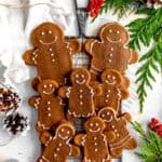 Gingerbread people on a wire cooling rack surrounded by pinecones and holly berries.